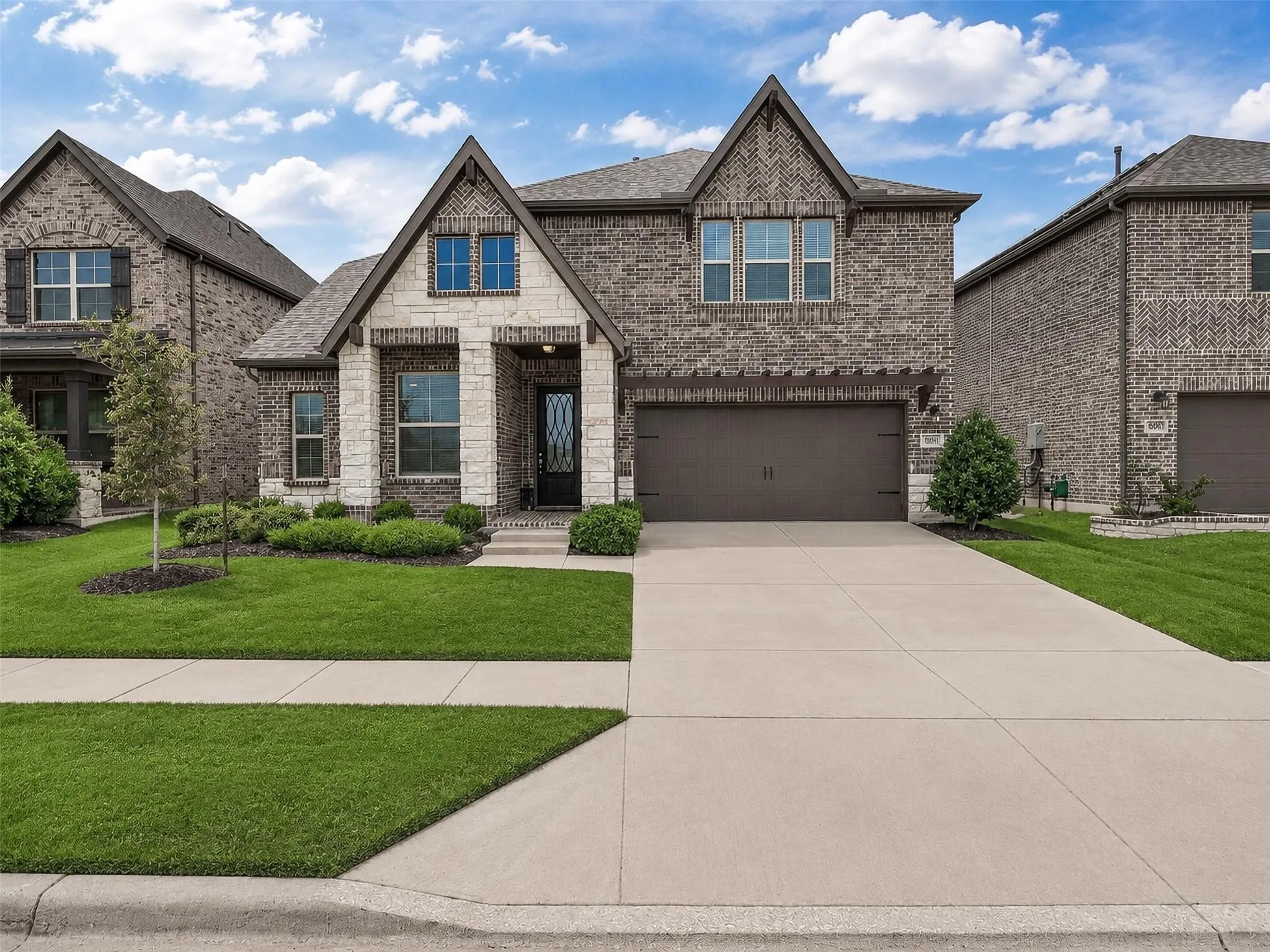 Brick and stone facade, gabled roofline, integrated two-car garage, concrete driveway, and established front landscaping