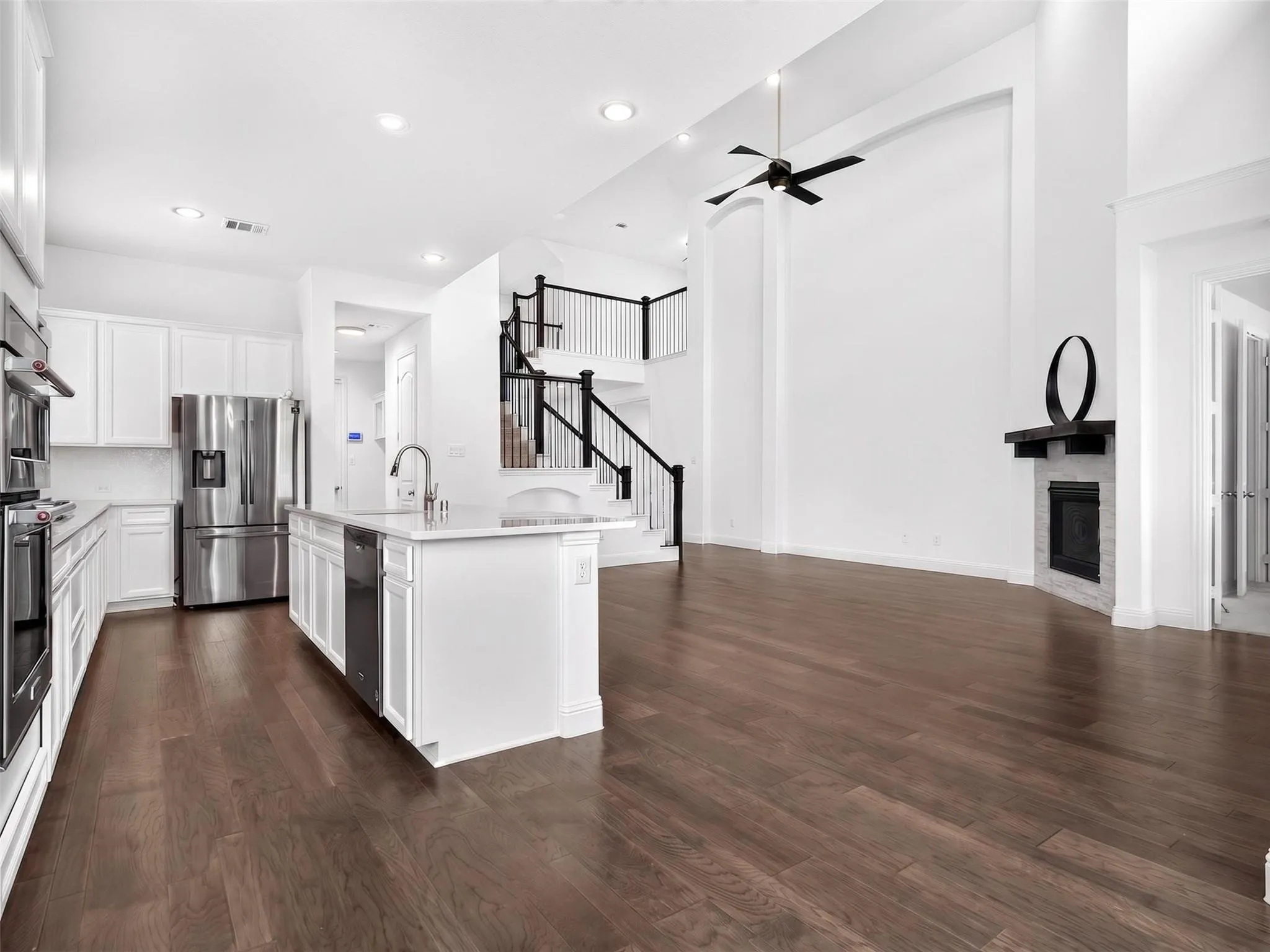 Expansive living area with wood-finish flooring, a fireplace, and a high ceiling with an attached fan