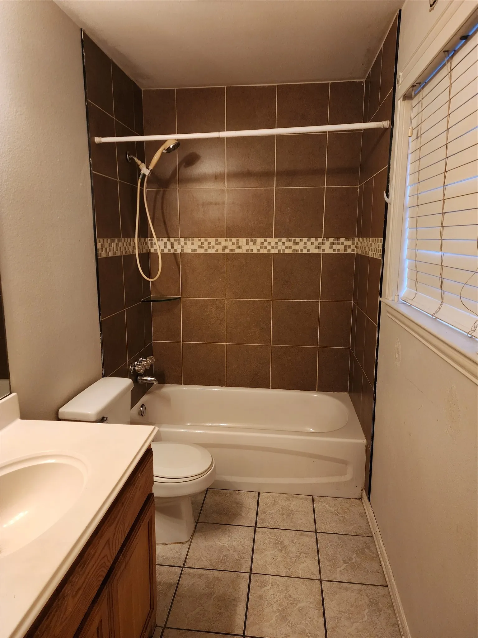 Bathroom featuring a tiled shower surround with decorative accent, a white bathtub, and a window with blinds