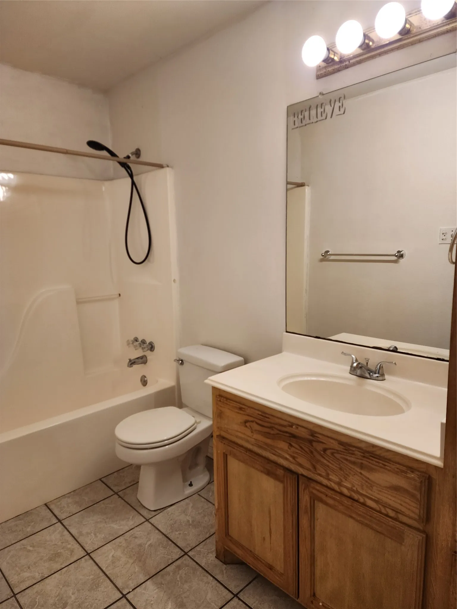 Bathroom featuring a white bathtub with shower, toilet, wood-finish vanity with an integrated sink, and a wall-mounted mirror with overhead lighting