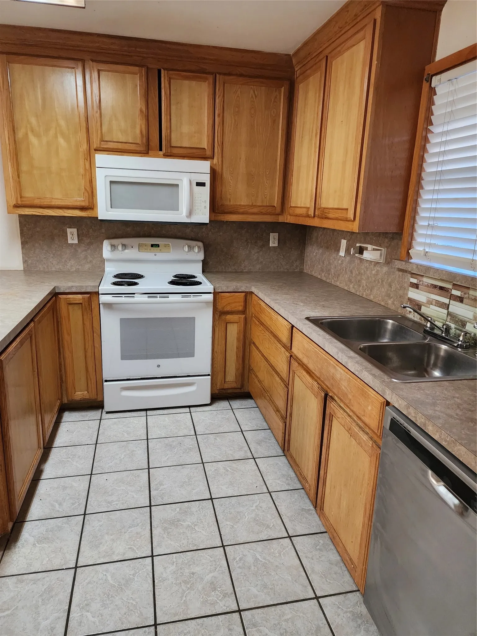 U-shaped kitchen featuring wood cabinetry, integrated stainless-steel dishwasher, and tile flooring