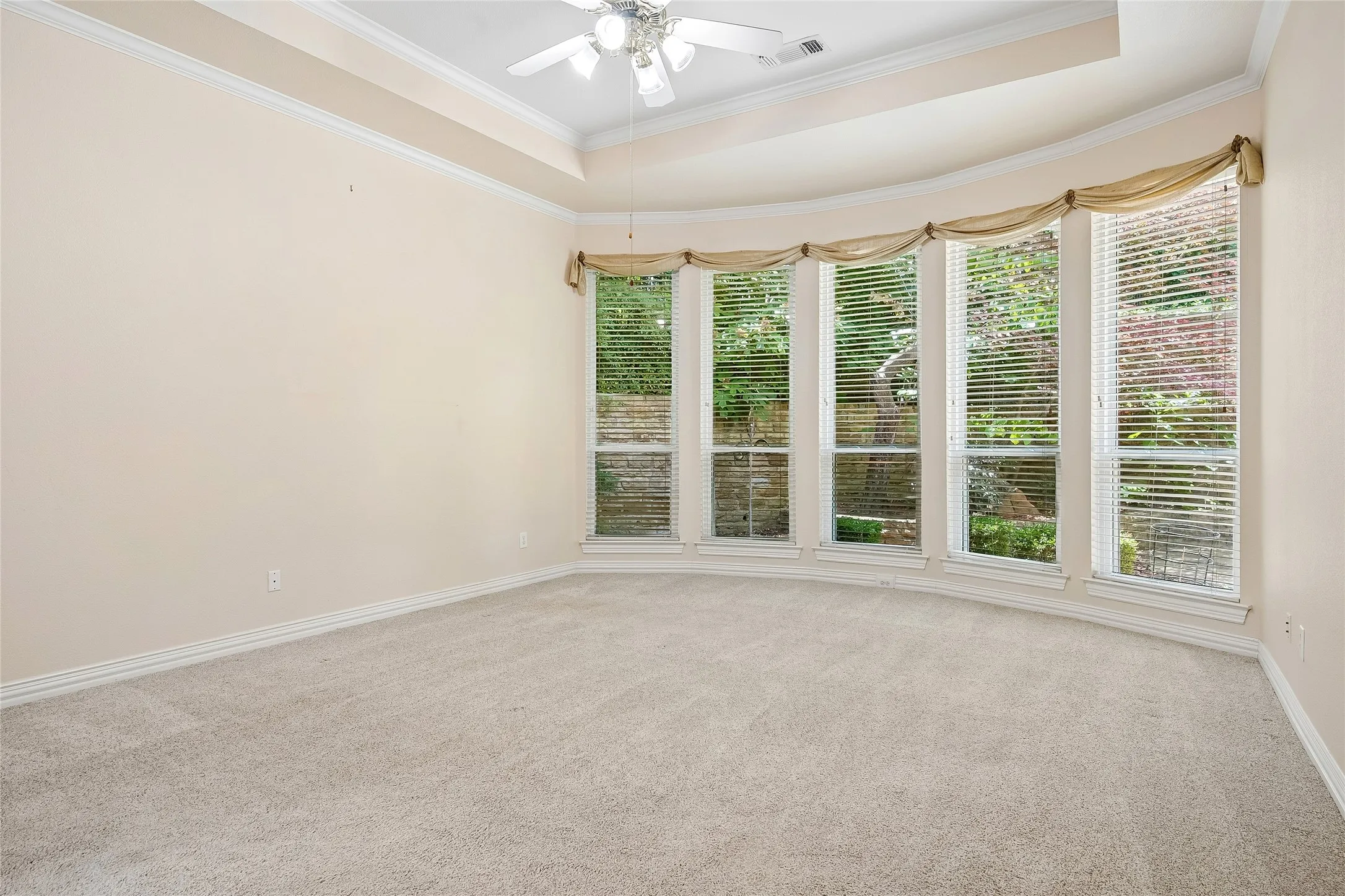 Huge Primary bedroom with curved wall of windows, tray ceiling, ceiling fan.