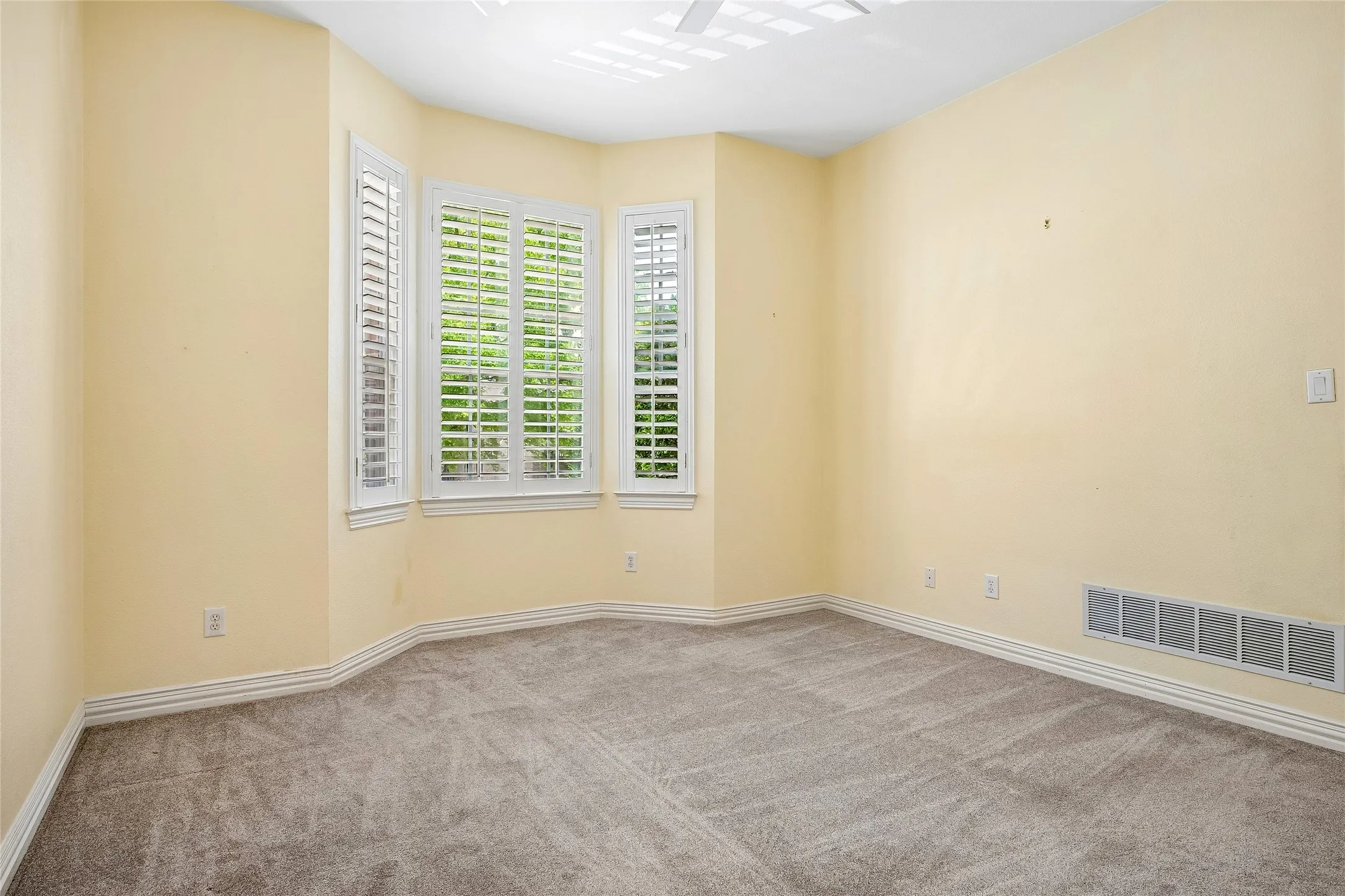 Large secondary bedroom with bay window, shutters, ceiling fan.