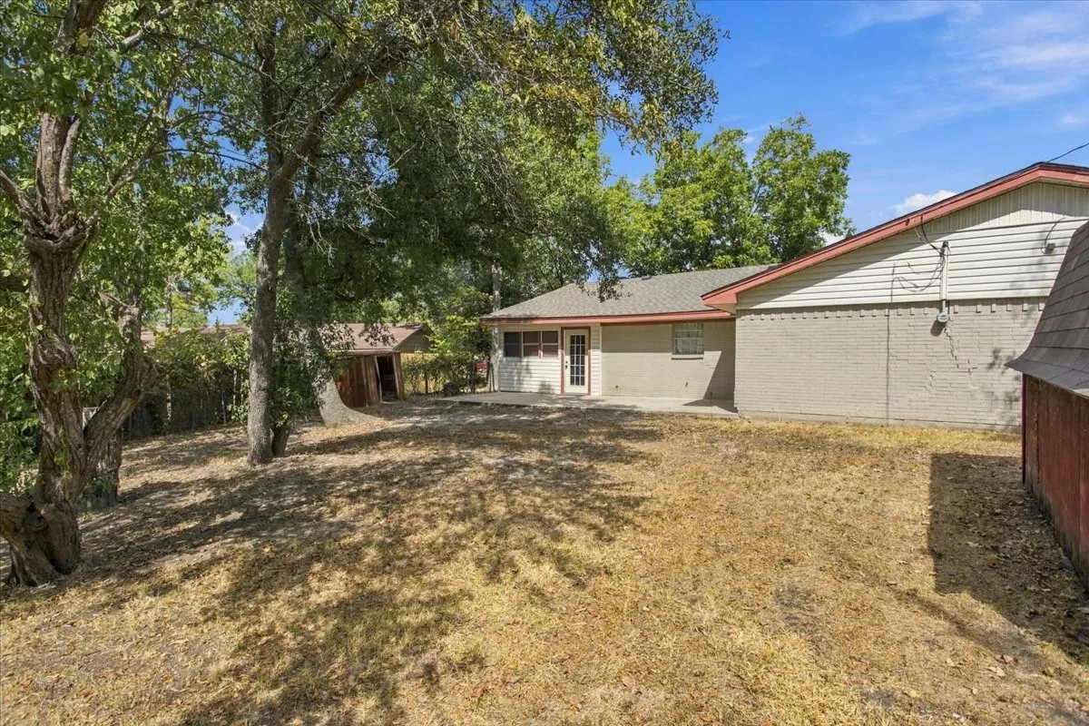 Partial view of treed back yard with sunroom entrance, large concrete back patio; storage building