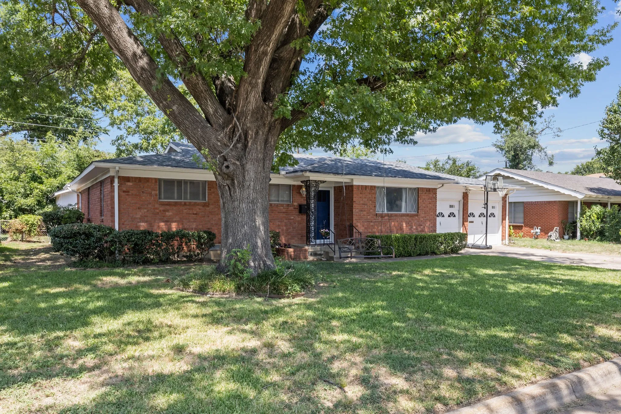 Brick exterior with a mature shade tree, manicured front lawn, and established shrubbery