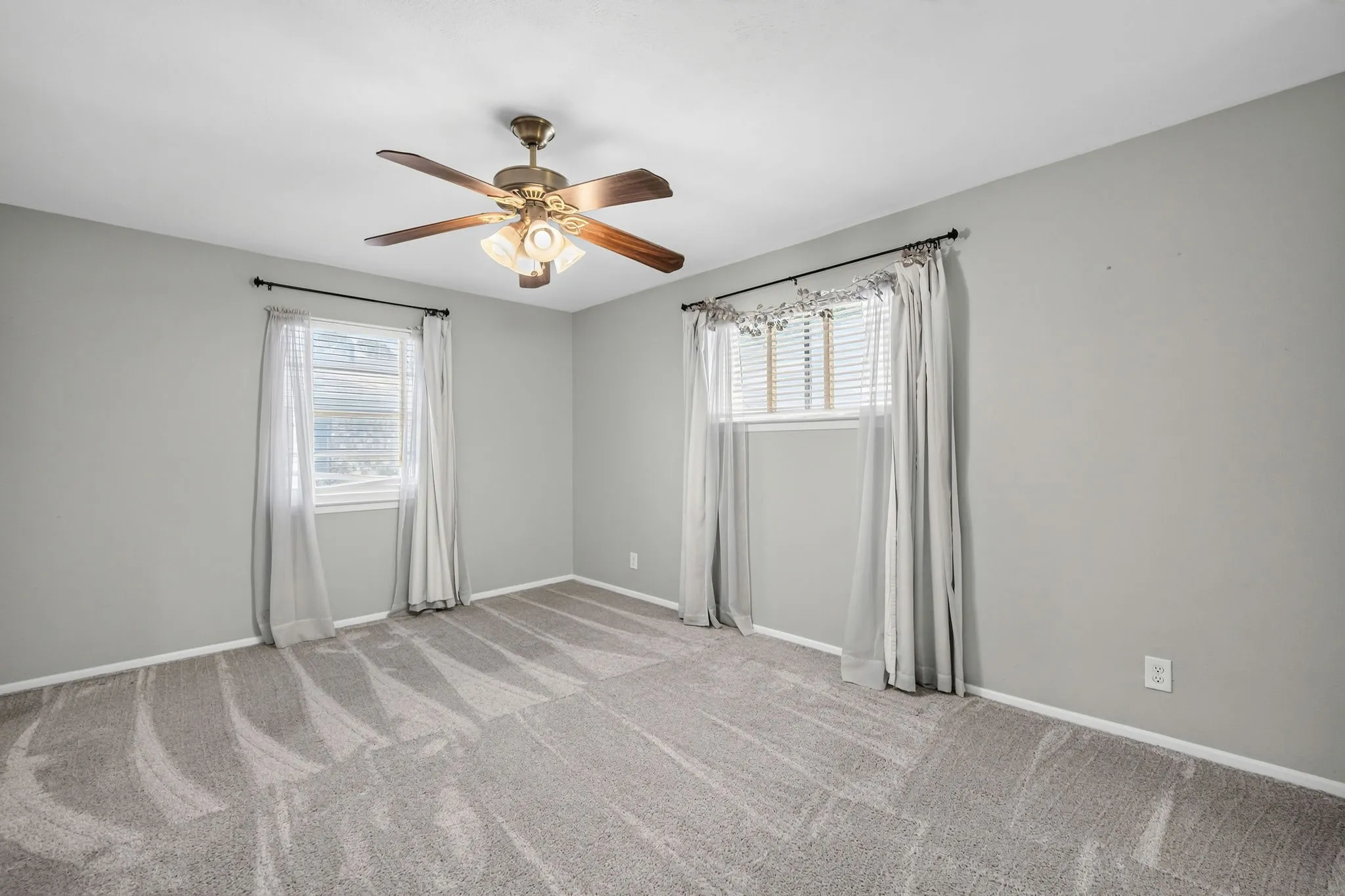 Spacious room featuring patterned carpeting, two windows with blinds, and a ceiling fan with integrated lighting