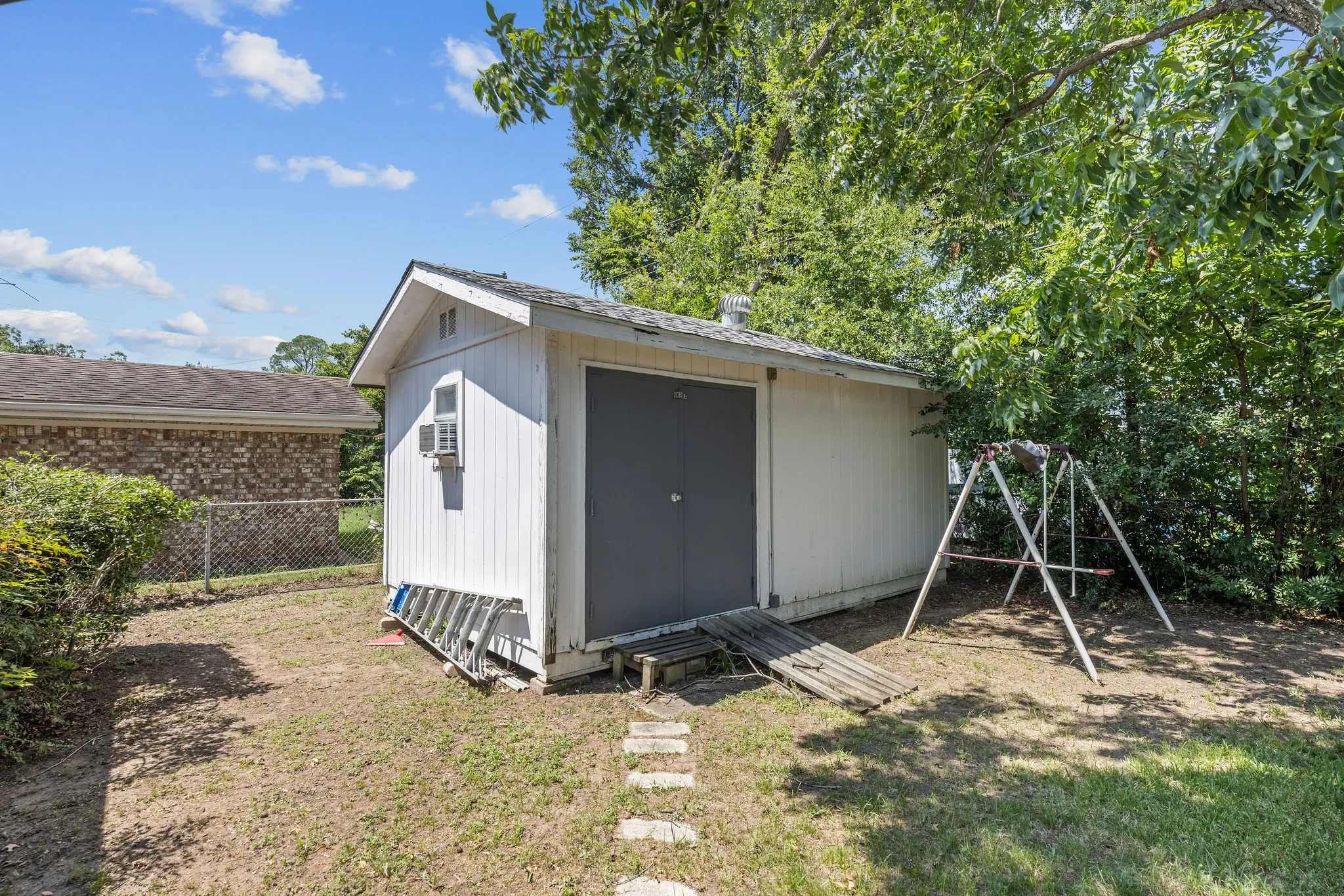 White storage shed with a dark gray door and a small window air conditioning unit