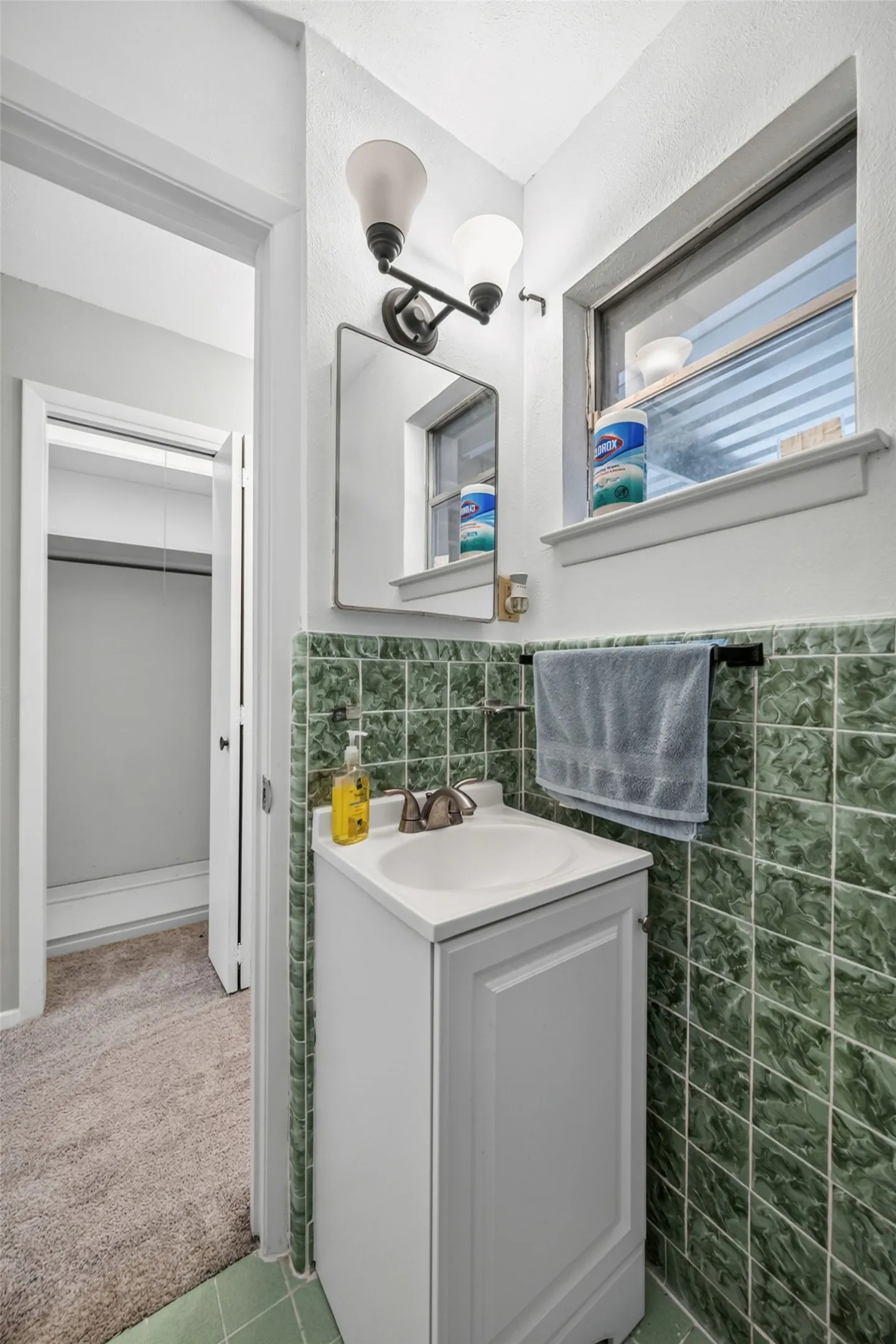 Bathroom featuring green ceramic wall tile, a white vanity with an integrated sink, a rectangular framed mirror, and a two-light vanity fixture
