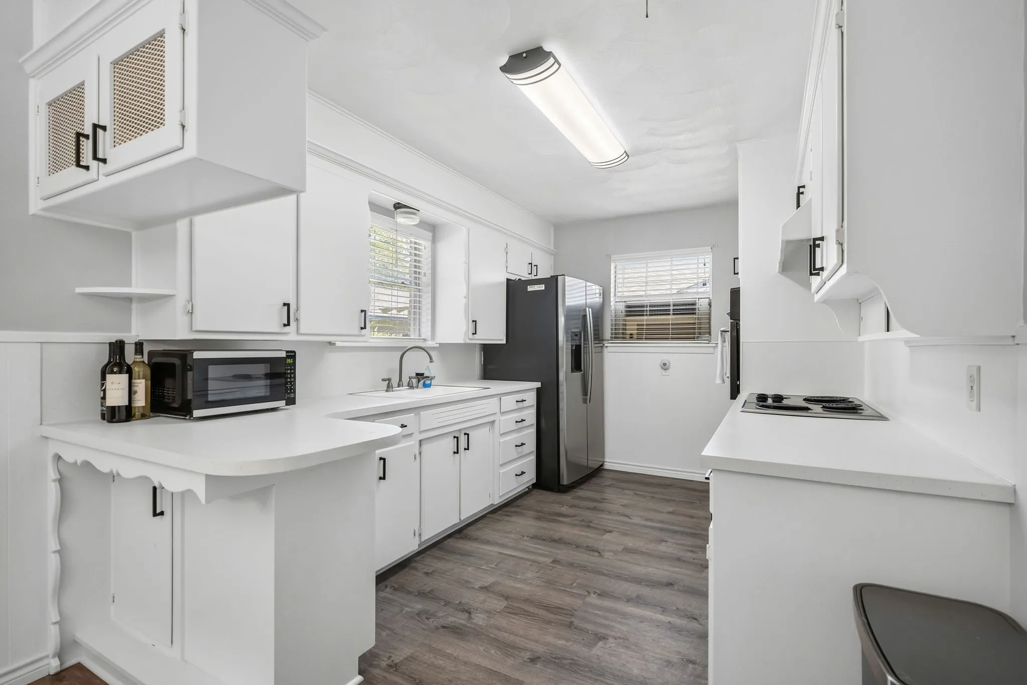 Kitchen featuring white cabinetry with black hardware, wood-finish flooring, and white countertops
