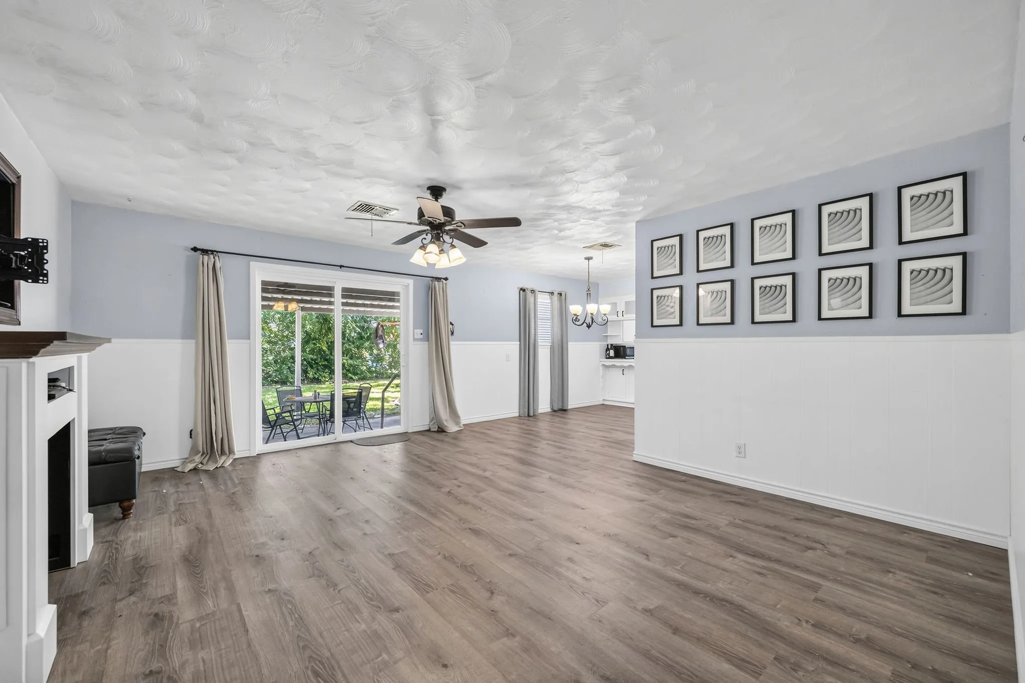Spacious living area featuring wood-finish flooring, a fireplace with a white mantel, and a ceiling fan with integrated lighting