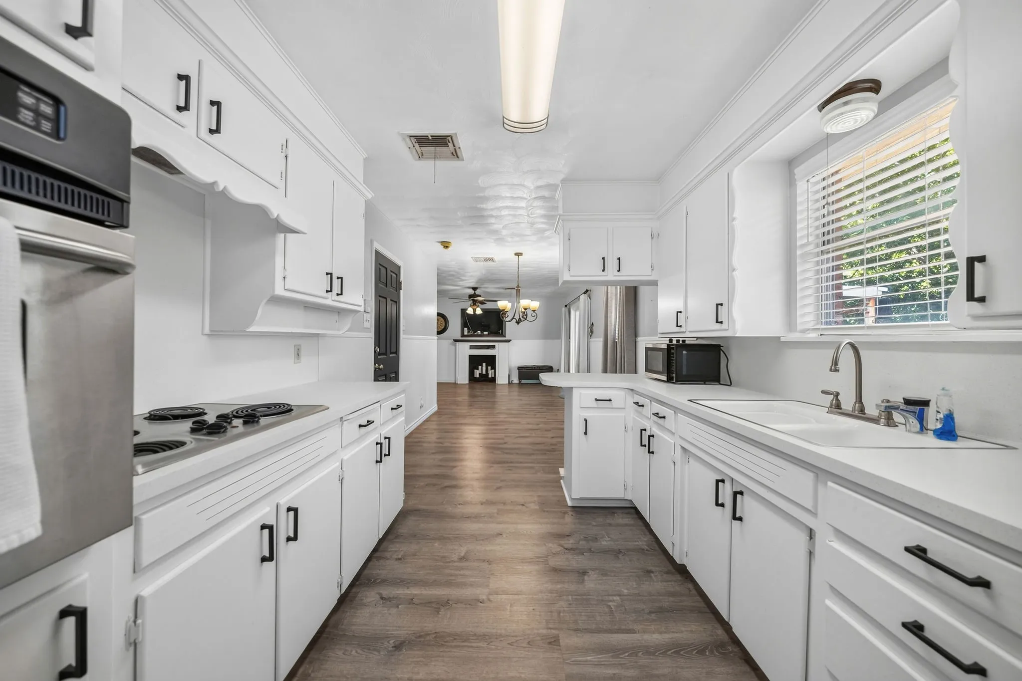 Galley kitchen featuring white cabinetry, integrated cooktop, built-in oven, and wood-finish flooring