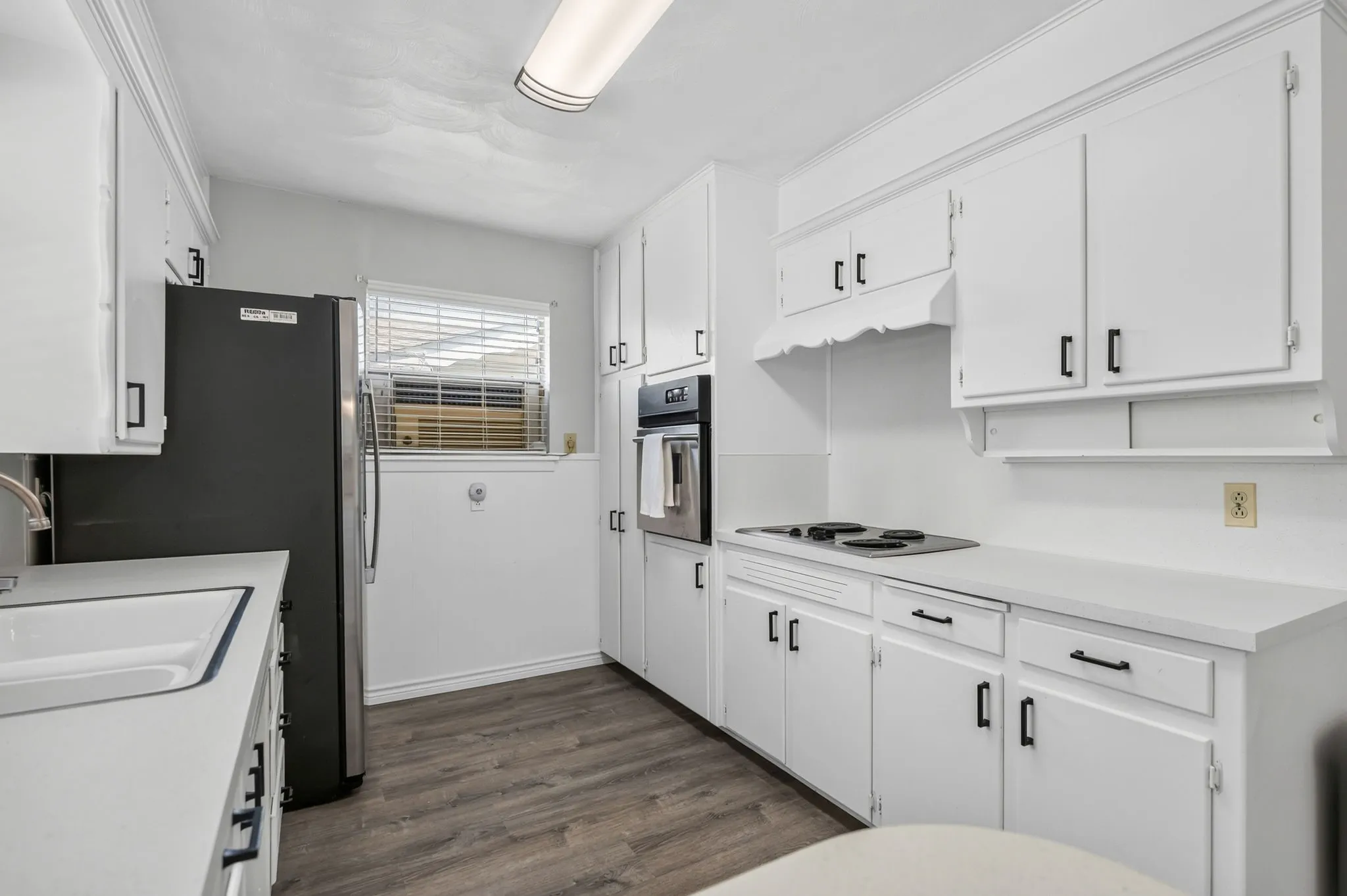 Kitchen featuring white cabinetry with black hardware, wood-finish flooring, white countertops, built-in oven, and a surface cooktop