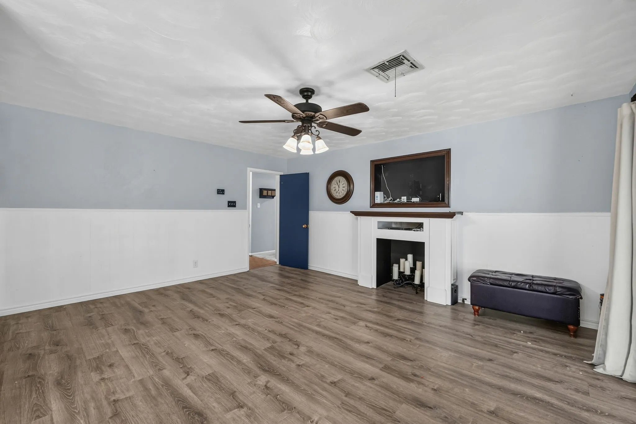 Spacious room featuring wood-finish flooring, wainscoting, and a ceiling fan with integrated lighting
