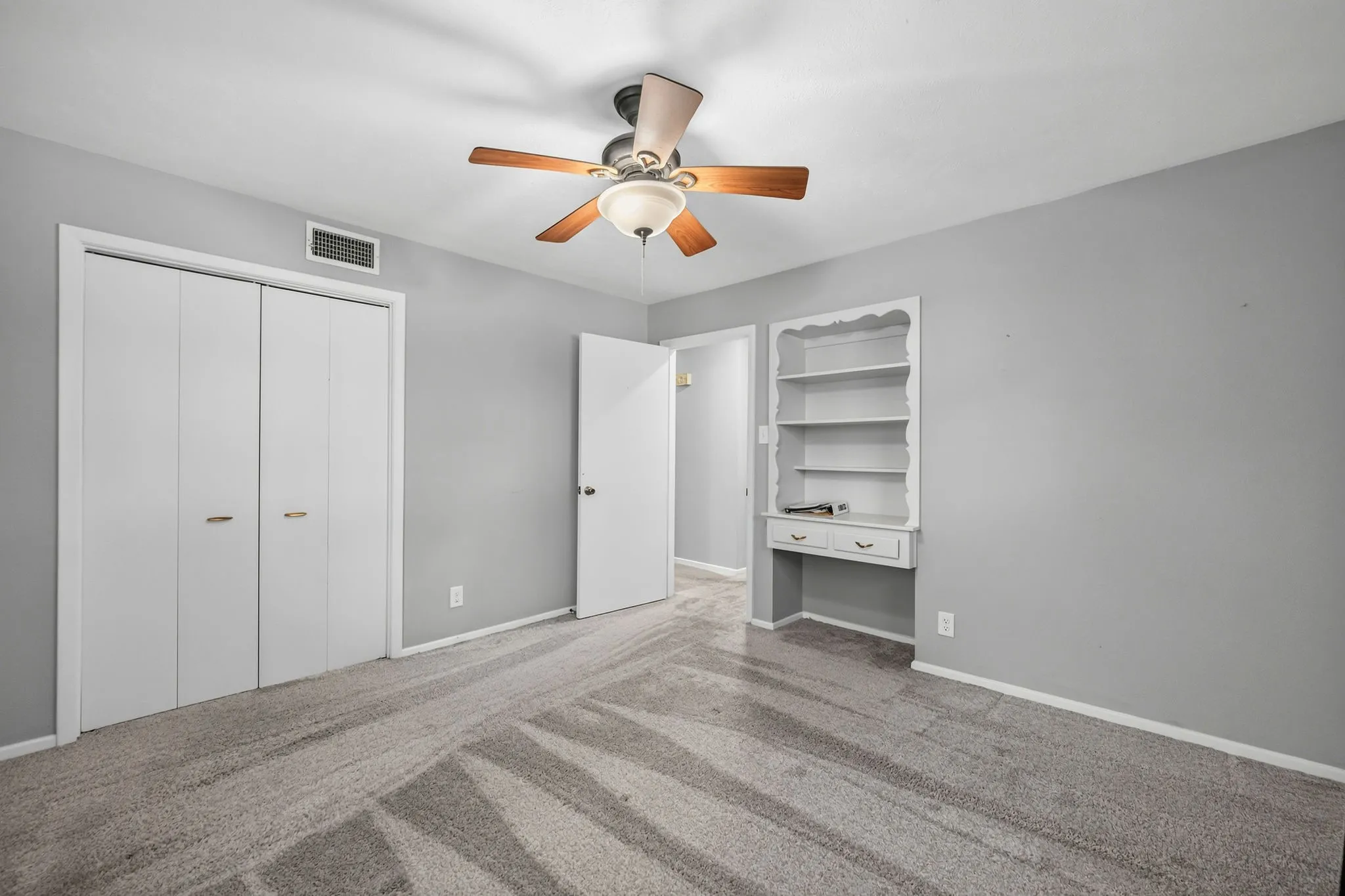 Carpeted room featuring light gray walls, a ceiling fan with wood-finish blades, and white bi-fold closet doors