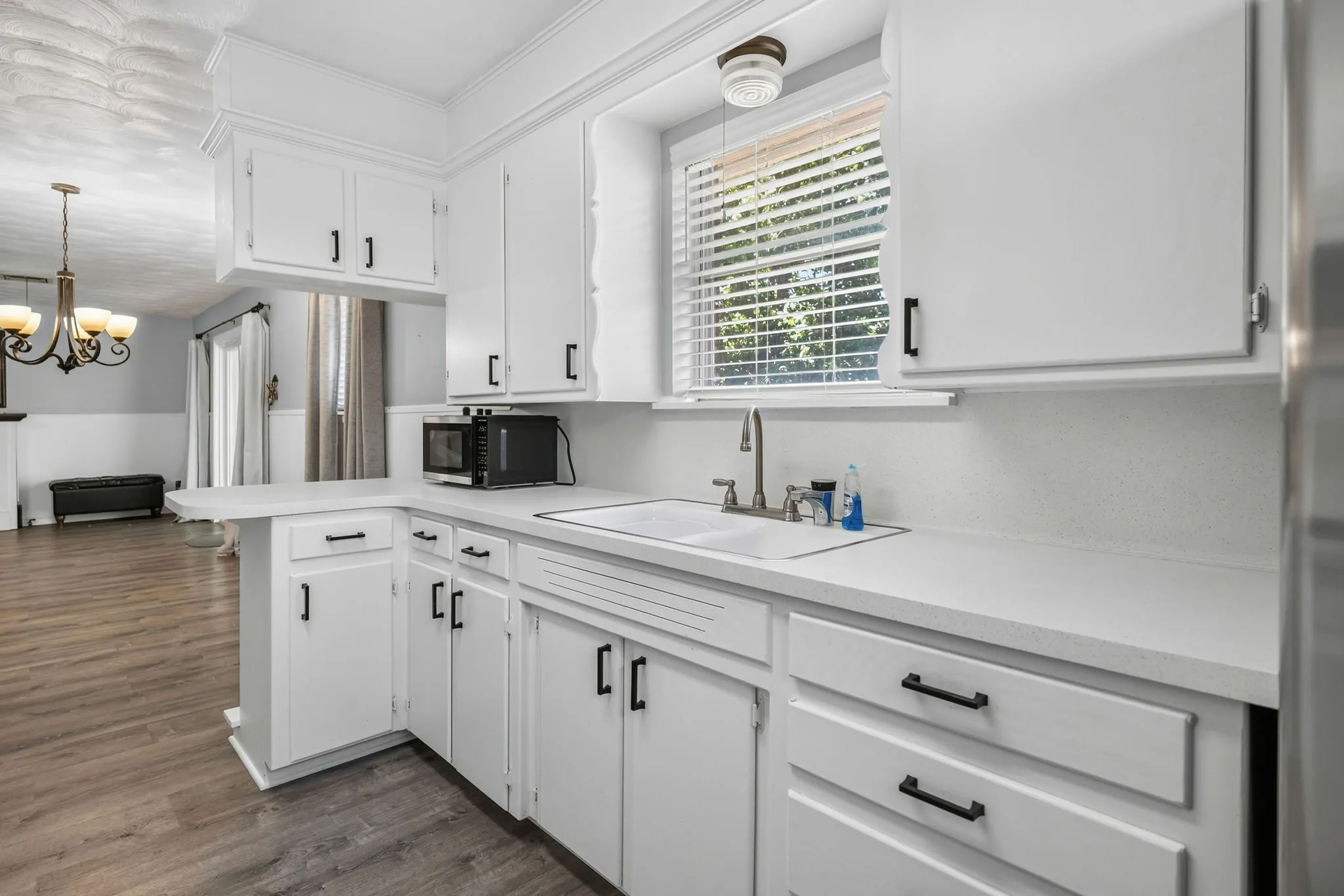 Kitchen featuring white cabinetry with dark hardware, a white composite sink, and light-toned countertops