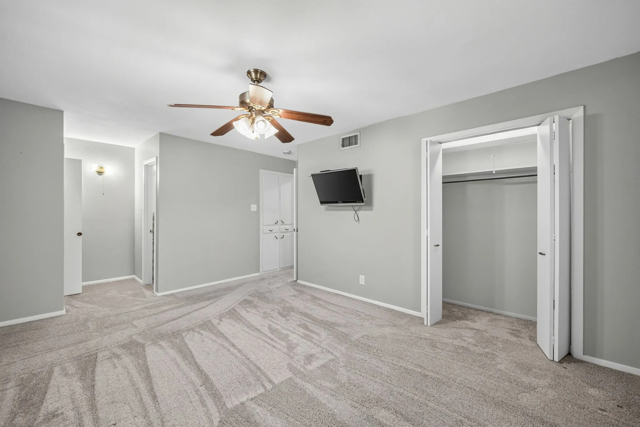Spacious room featuring light gray walls, textured carpeting, and a ceiling fan with integrated lighting