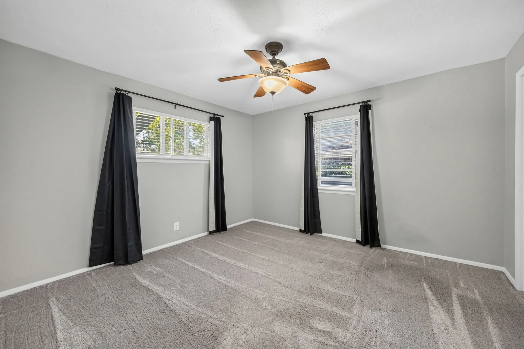 Carpeted room featuring a ceiling fan with integrated lighting, two windows with blinds, and light gray wall paint