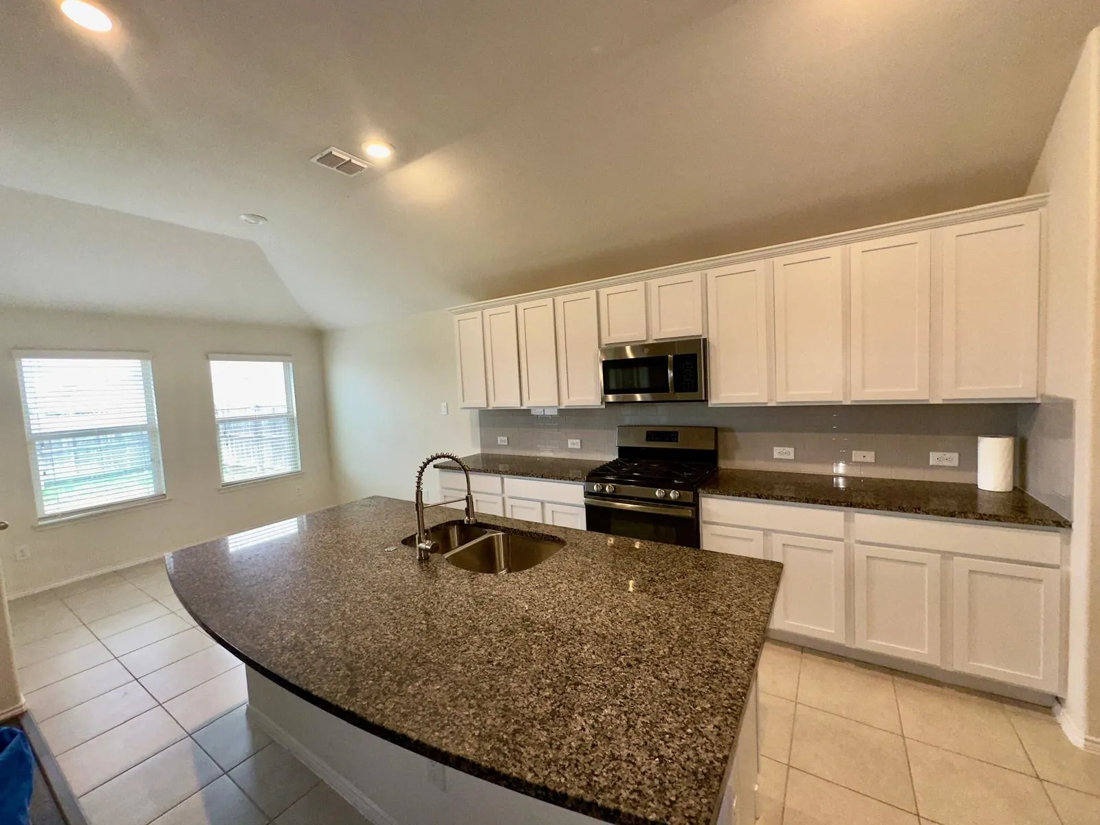 Kitchen with white cabinetry, appliances with stainless steel finishes, vaulted ceiling, sink, and an island with sink
