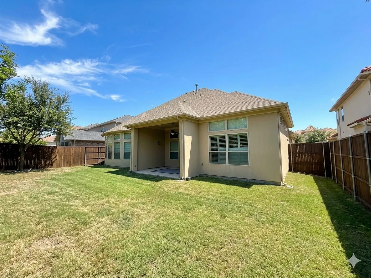 Expansive grassy yard with wood fencing, a covered patio, and stucco exterior