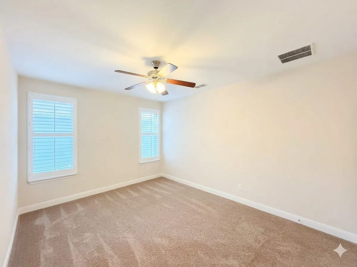 Neutral wall tones, carpeted flooring, two windows with louvered shutters, and a ceiling fan with integrated lighting