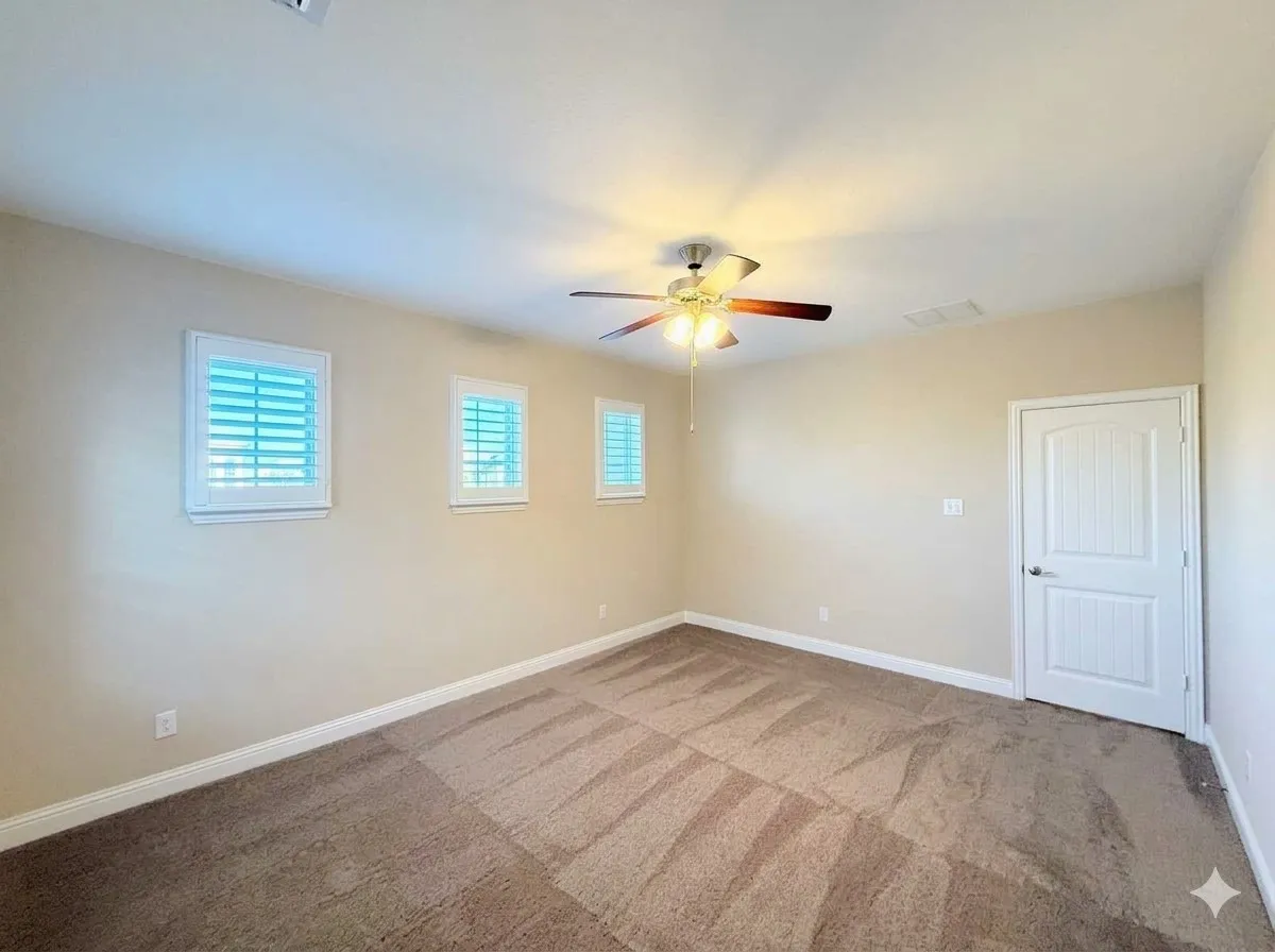 Carpeted flooring, three windows with white plantation shutters, white paneled door, and a ceiling fan with integrated lighting