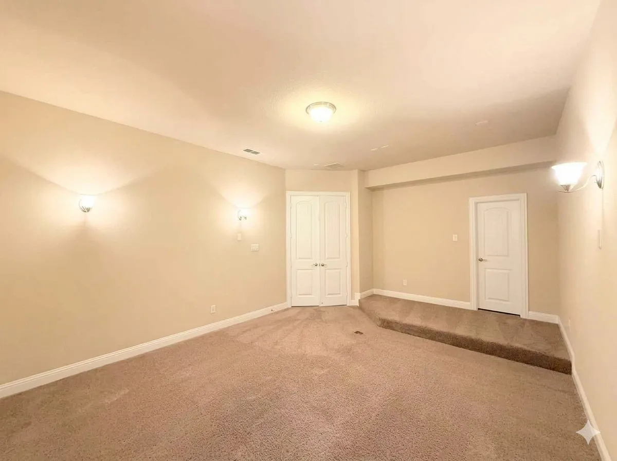 Carpeted room with a raised platform, two wall sconces, a ceiling-mounted light fixture, and two white panel doors