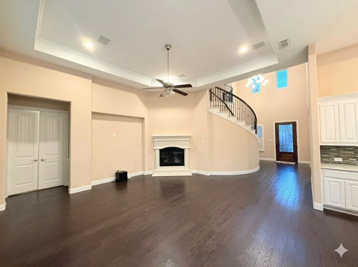 Dark wood-finish flooring, a curved staircase with wrought iron balusters, a fireplace with a white mantel, white cabinetry with a tile backsplash, and a tray ceiling