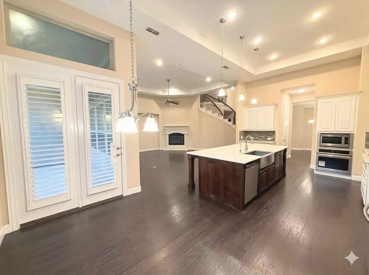 Spacious open-concept interior featuring wood-finish flooring, a kitchen island with a farmhouse sink, integrated stainless steel appliances, and a curved staircase