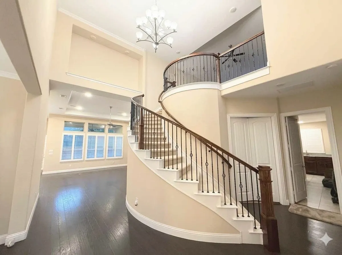 Curved staircase with decorative wrought iron spindles, wood-finish flooring, and high ceilings with an ornate chandelier