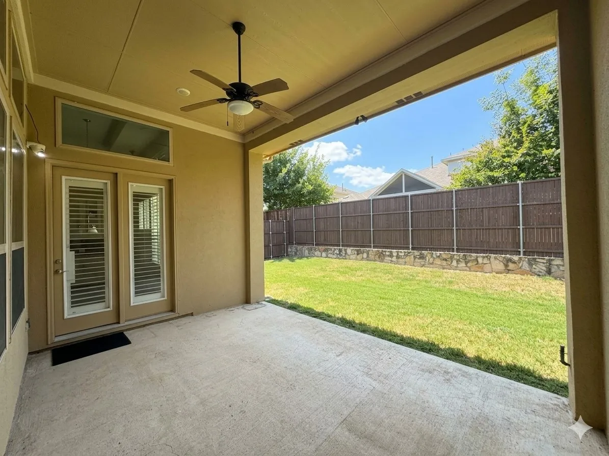 Covered patio with a ceiling fan, concrete flooring, and direct access to a fenced yard featuring a stone retaining wall
