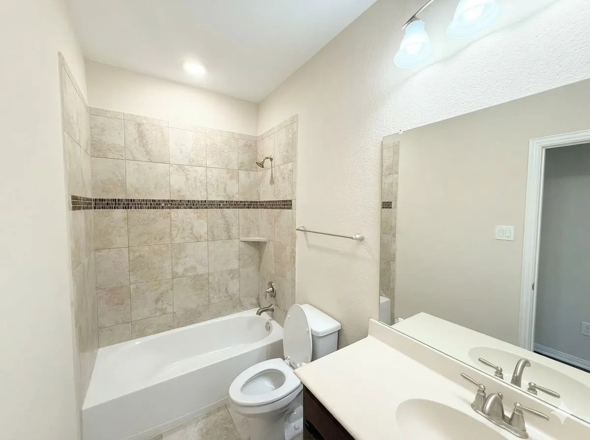 Bathtub with tiled surround featuring a decorative mosaic accent band and an integrated shelf
