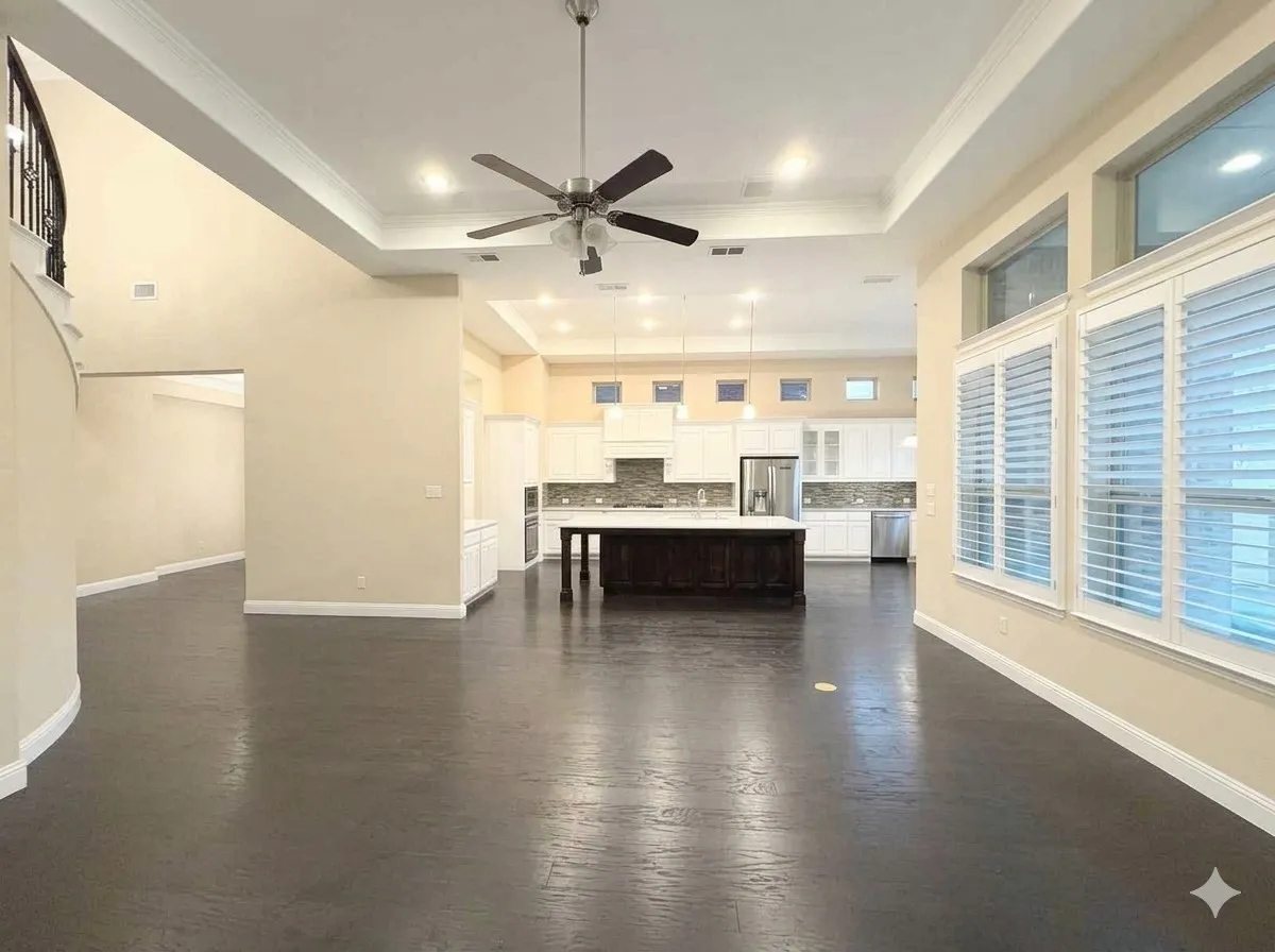 Spacious living area featuring dark wood-finish flooring, a tray ceiling with a ceiling fan, and large windows with plantation shutters