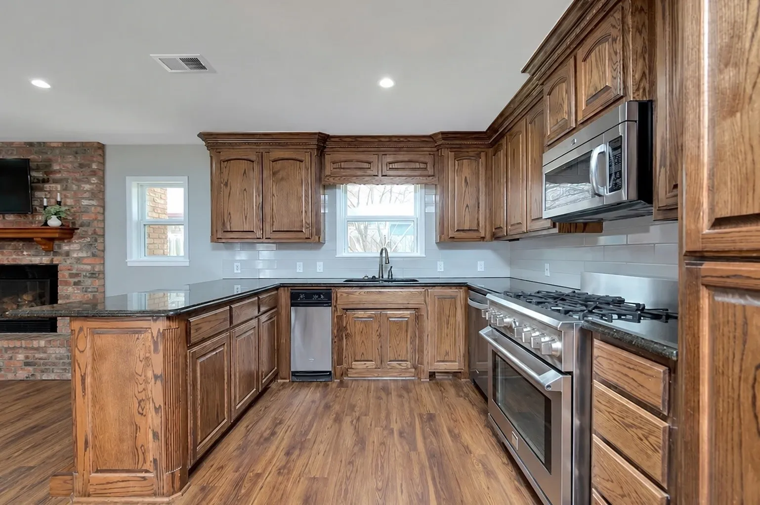 Wood-finish flooring, dark wood cabinetry, black countertops, stainless steel appliances, and white subway tile backsplash