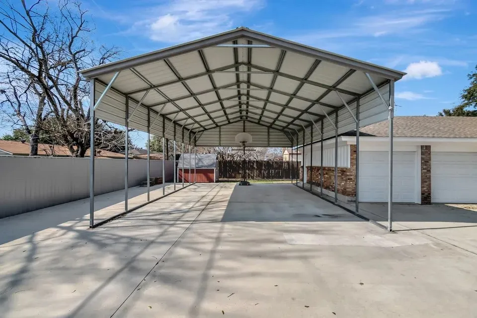 Expansive concrete driveway with a large metal carport structure