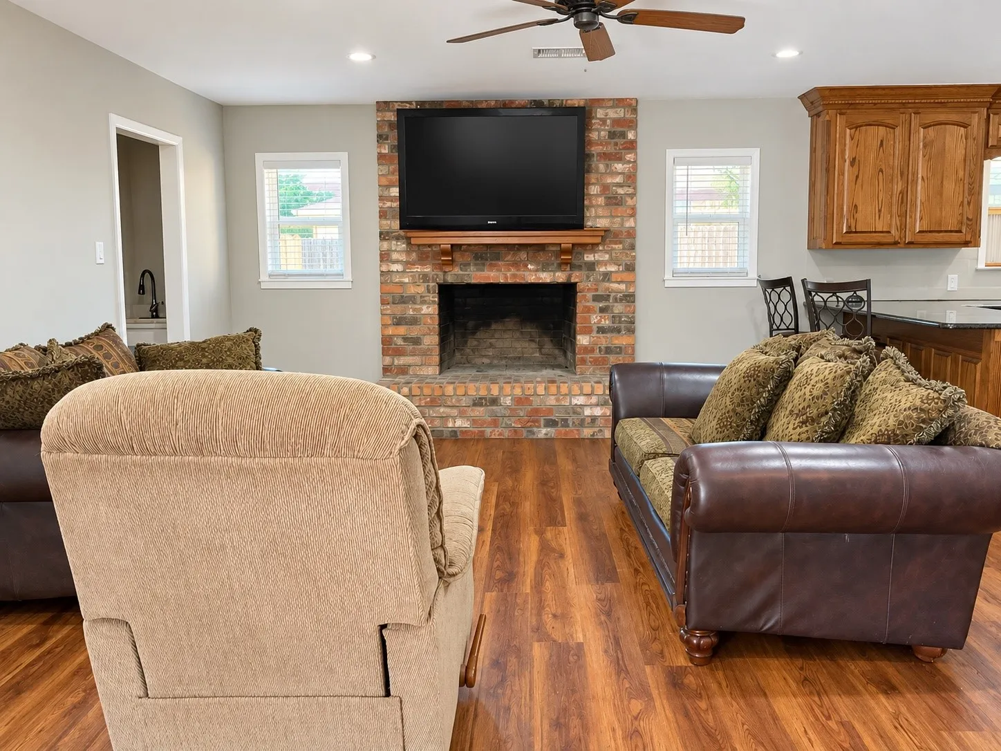 Brick fireplace with a wooden mantel, wood-finish flooring, recessed lighting, and a ceiling fan