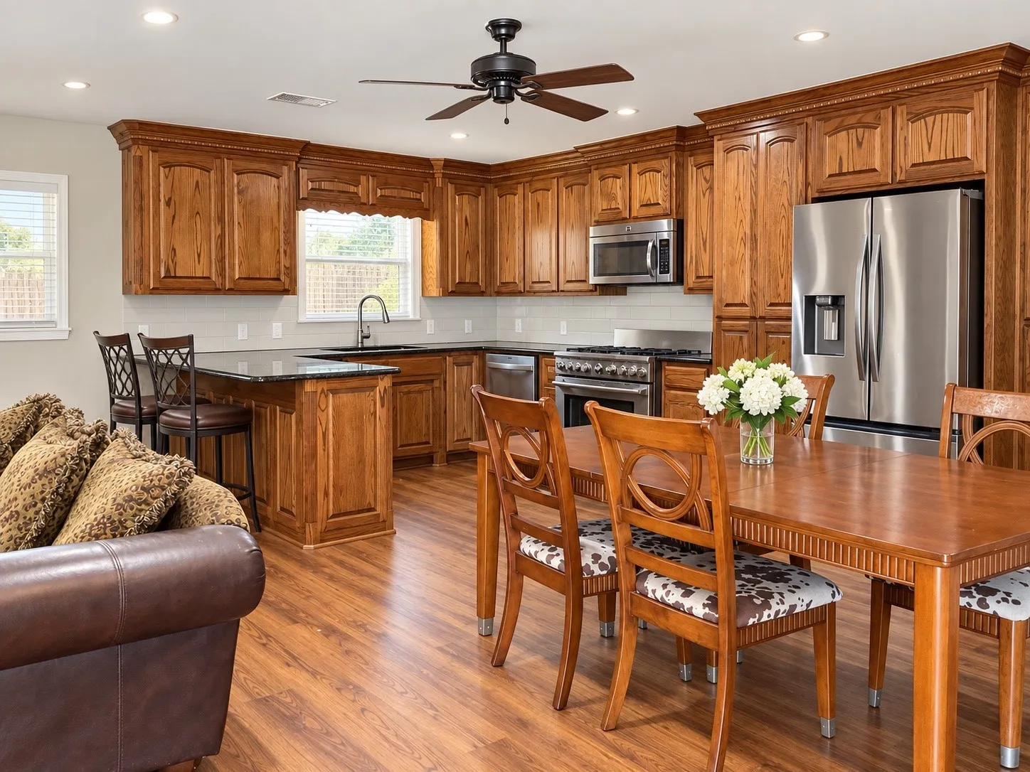 Hardwood-finish flooring throughout, wood cabinetry with crown molding, stainless steel appliances, recessed lighting, and a ceiling fan