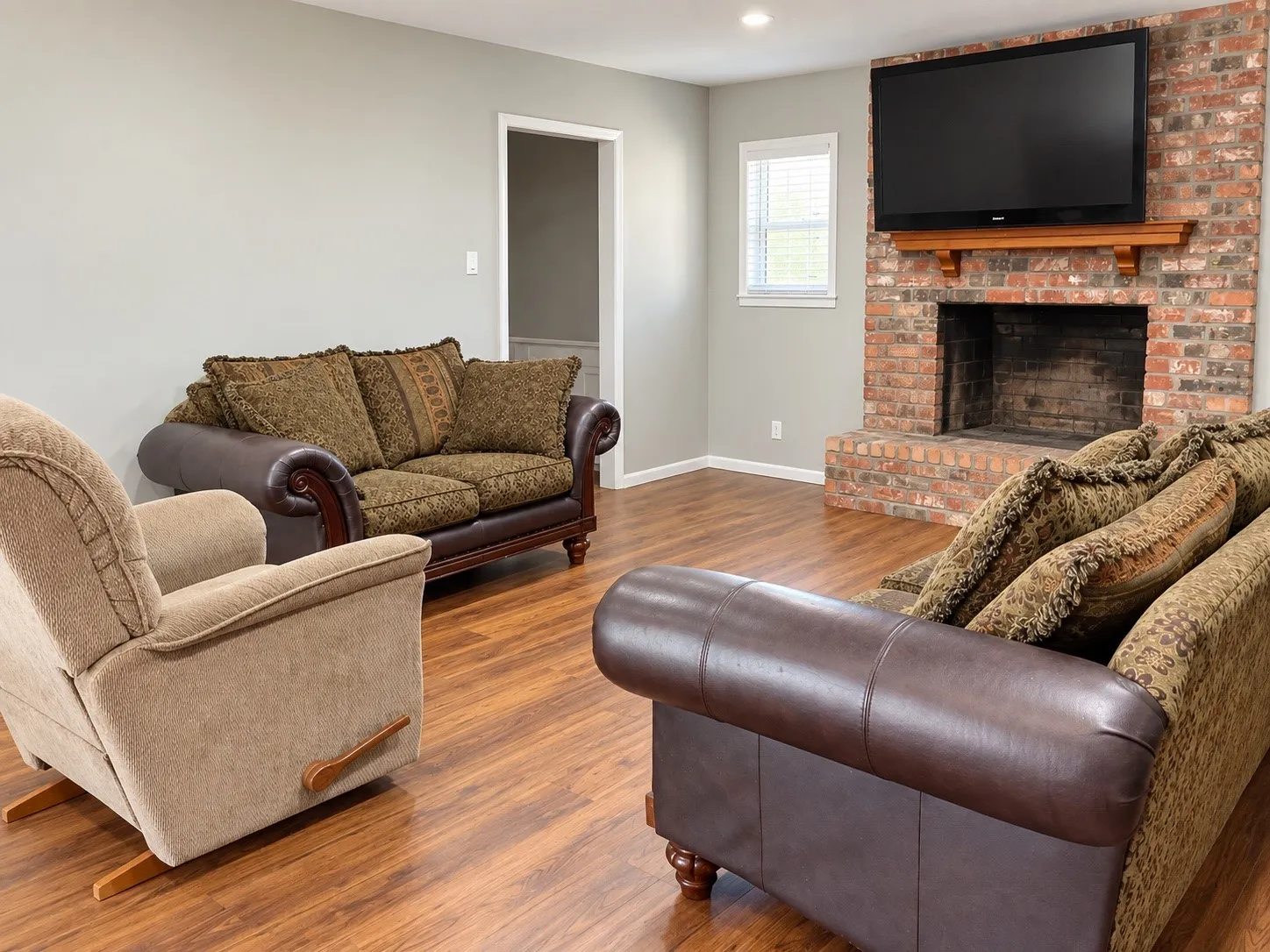 Brick-clad fireplace with a wood mantel, wood-finish flooring, and recessed lighting