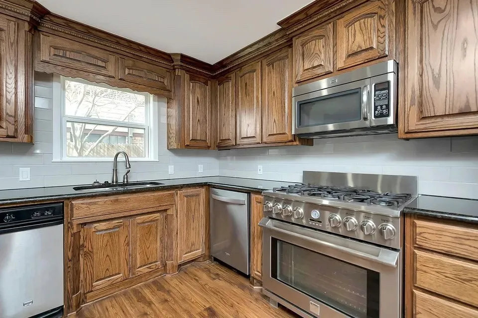 Wood-finish flooring, wood cabinetry, stainless steel appliances, dark countertops, and a subway tile backsplash