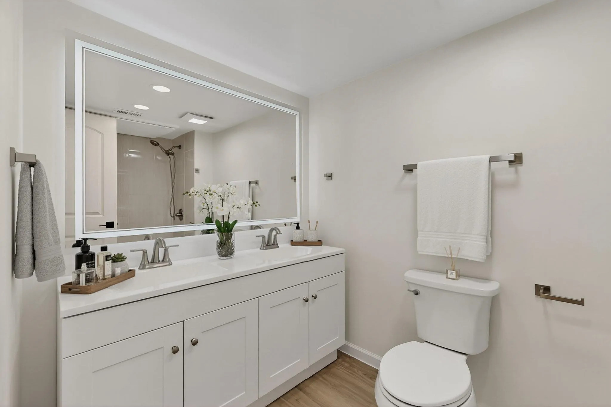 Dual vanity with white cabinetry and integrated sinks, brushed nickel fixtures, and a large illuminated mirror