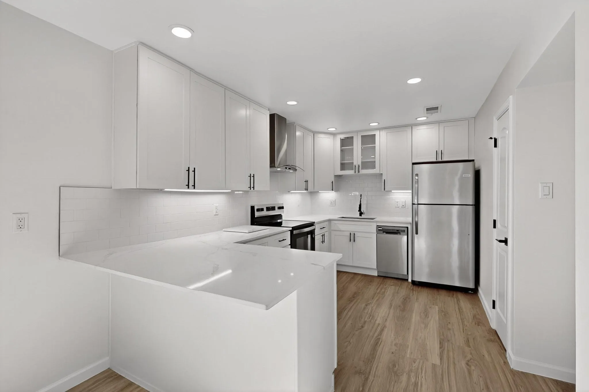 Modern kitchen featuring white shaker cabinetry, stainless steel appliances, white subway tile backsplash, light wood-finish flooring, and recessed lighting