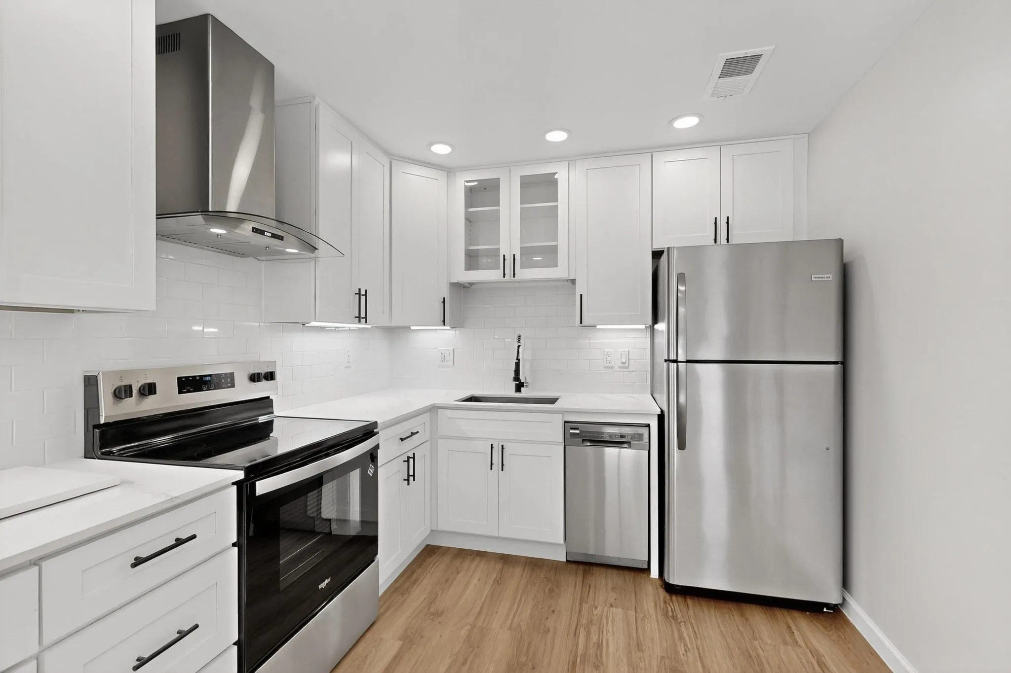 White shaker cabinetry, stainless steel appliances, solid surface countertops, subway tile backsplash, and wood-finish flooring