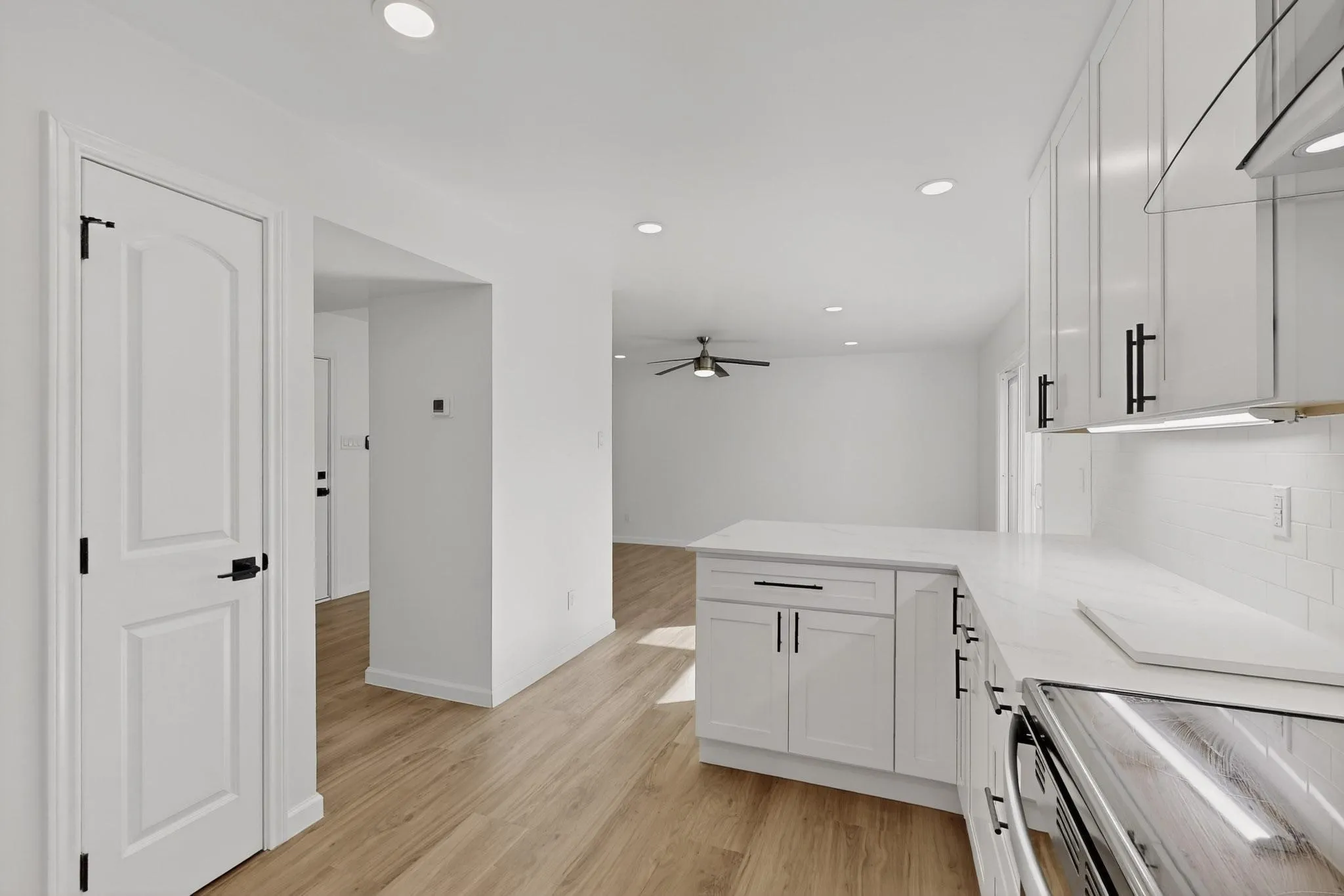Kitchen featuring white cabinetry, light-colored countertops, a tile backsplash, wood-finish flooring, and recessed lighting