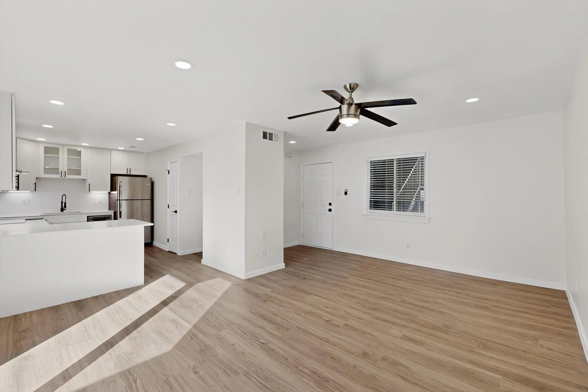 Light wood-finish flooring with recessed lighting and a ceiling fan