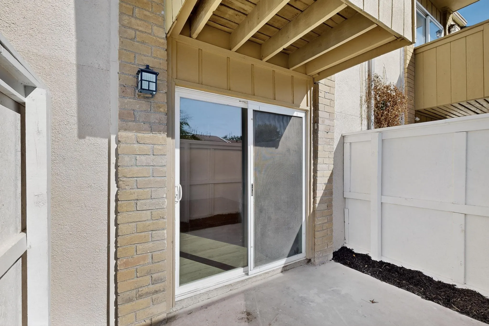 Outdoor concrete patio featuring a sliding glass door with screen, brick exterior accents, and a privacy fence