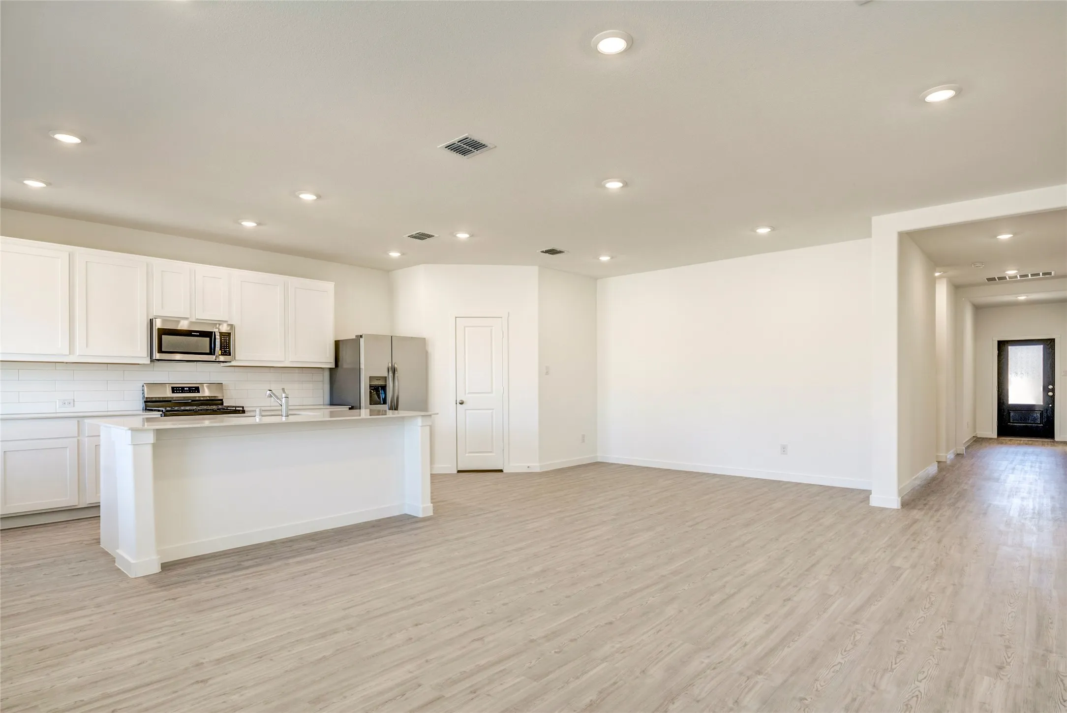Down the hall into the open-concept interior featuring light colored LVP flooring, recessed lighting, and a kitchen island with white cabinetry