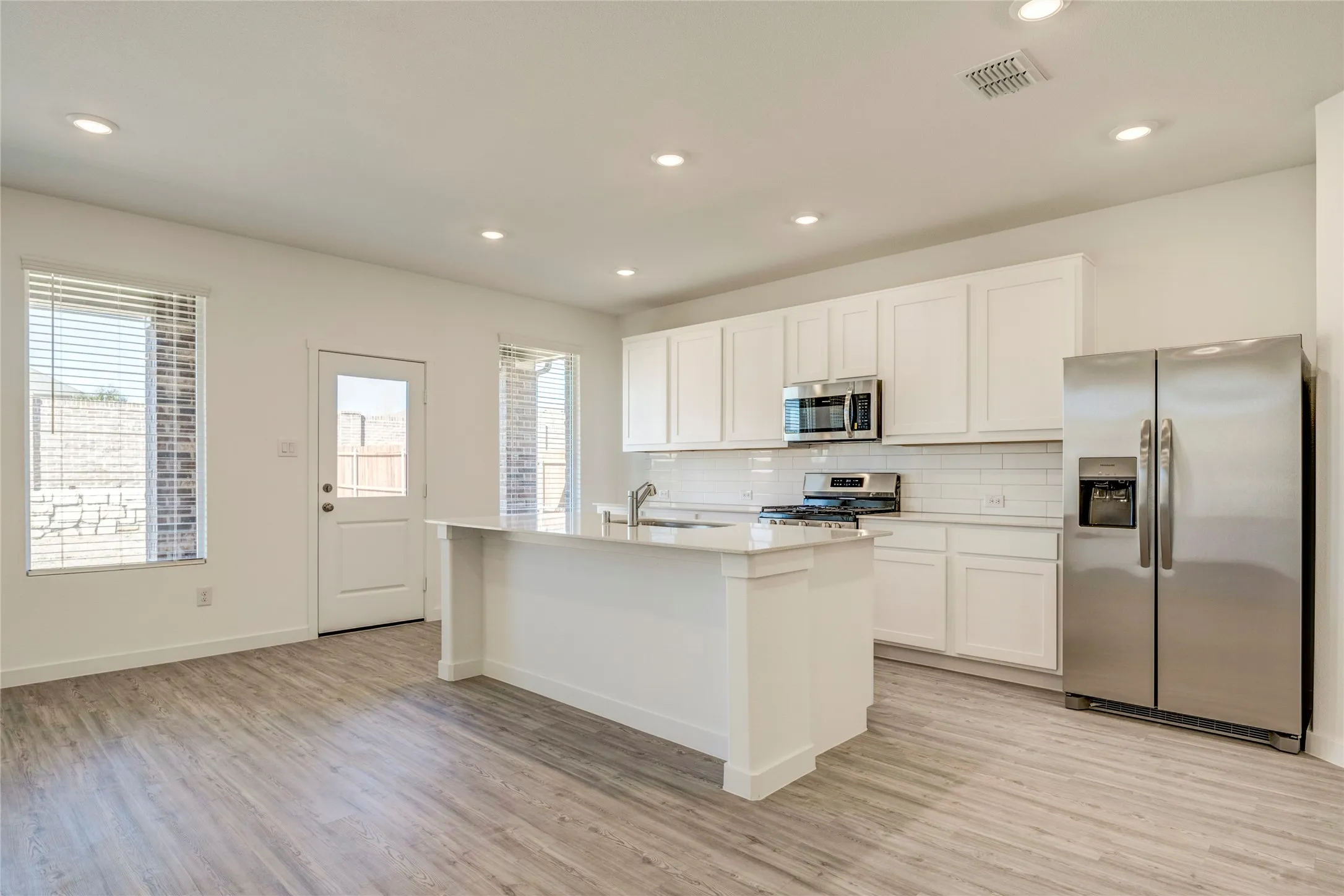 Spacious kitchen featuring white cabinetry, stainless steel appliances, a center island with sink, subway tile backsplash, and LVP flooring