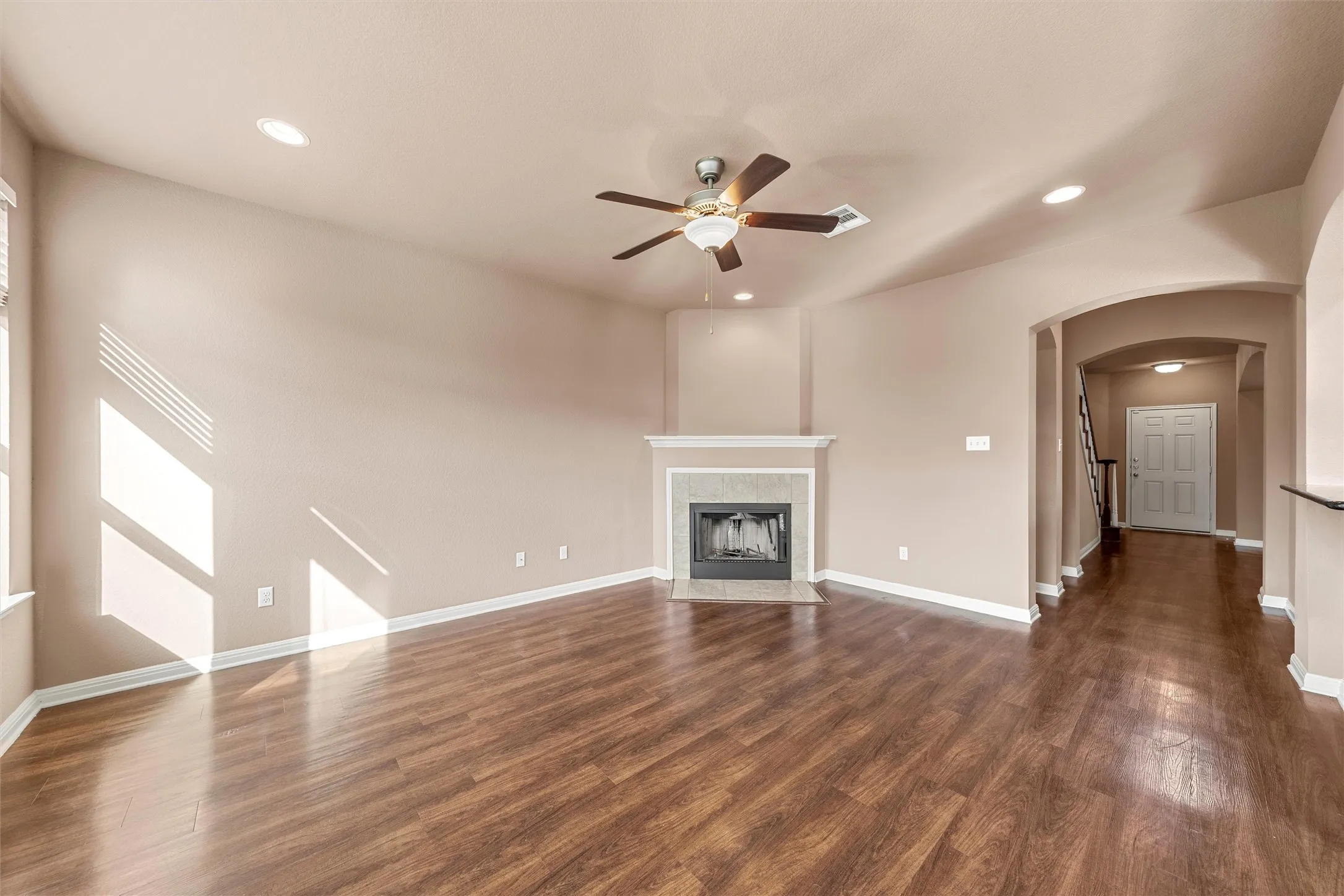 Vaulted ceiling, wood-finish flooring, recessed lighting, ceiling fan, and a fireplace with a stone surround