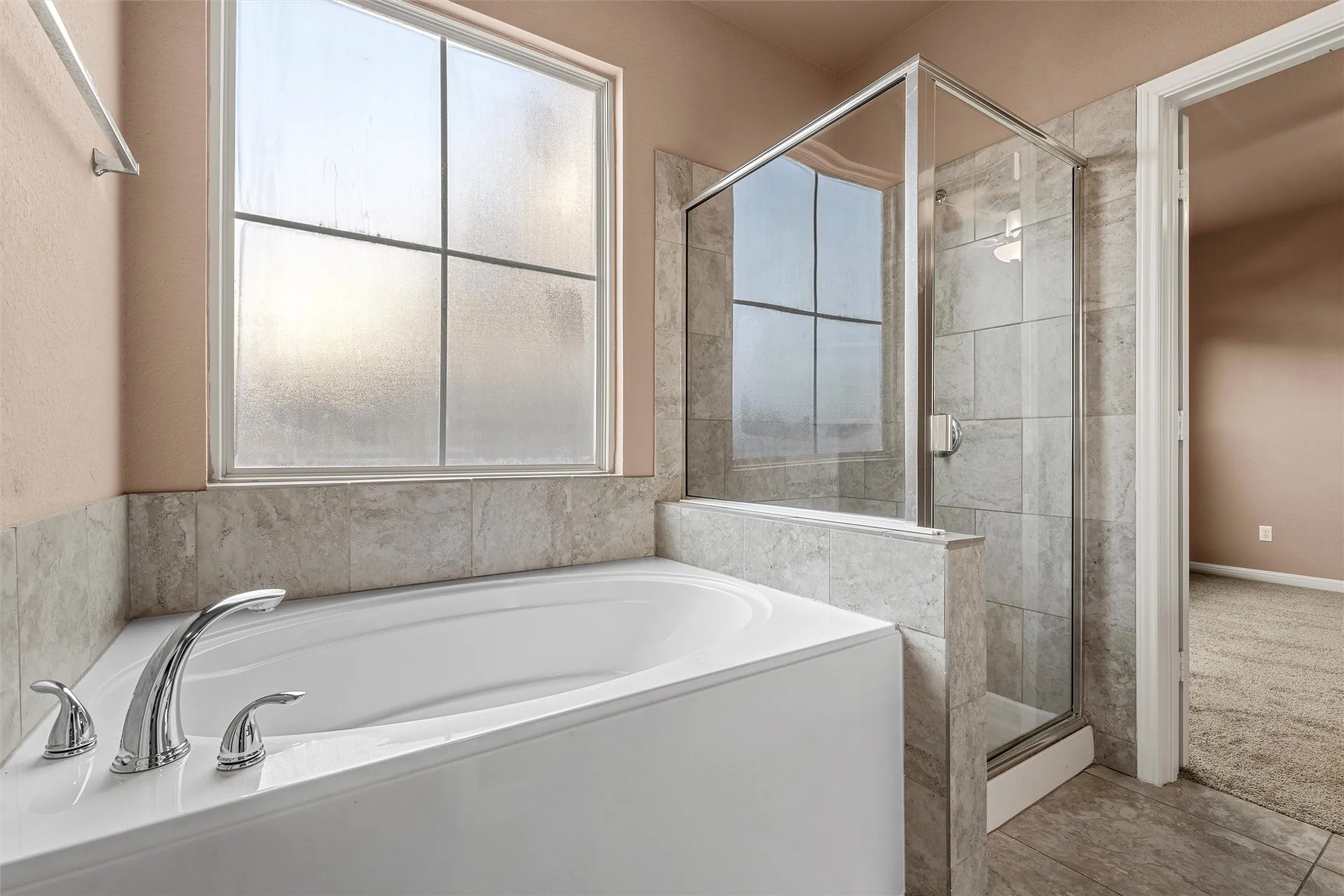 Soaking tub with chrome fixtures, glass-enclosed shower with tiled surround, tiled flooring, and a frosted window