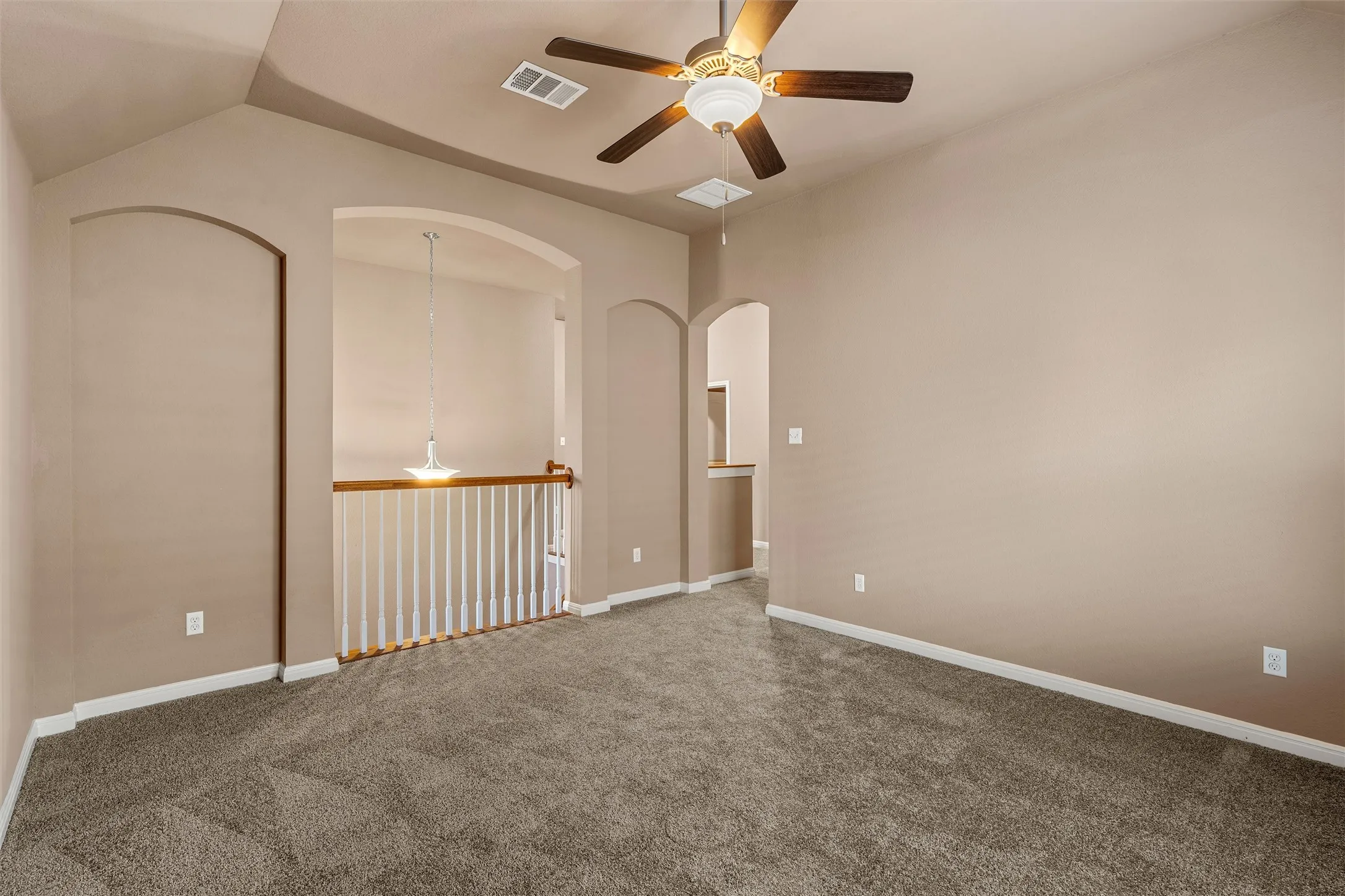 Vaulted ceiling with an attached ceiling fan, arched doorways, carpeted flooring, and a spindle railing with wood-finish top rail