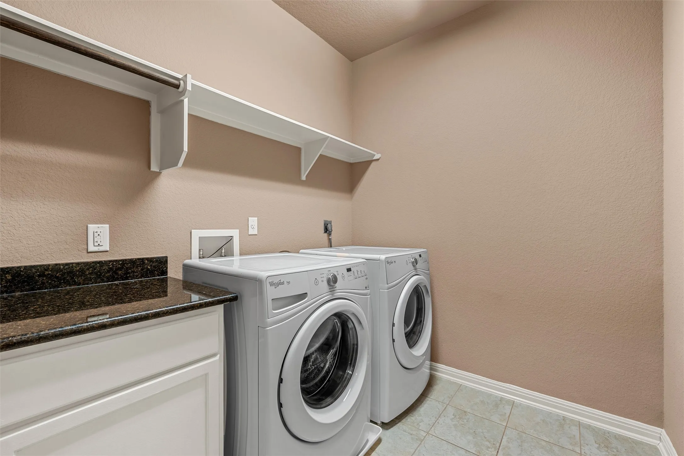 White shaker-style cabinetry with a polished dark stone countertop, white wall-mounted shelving, and a metal hanging rod